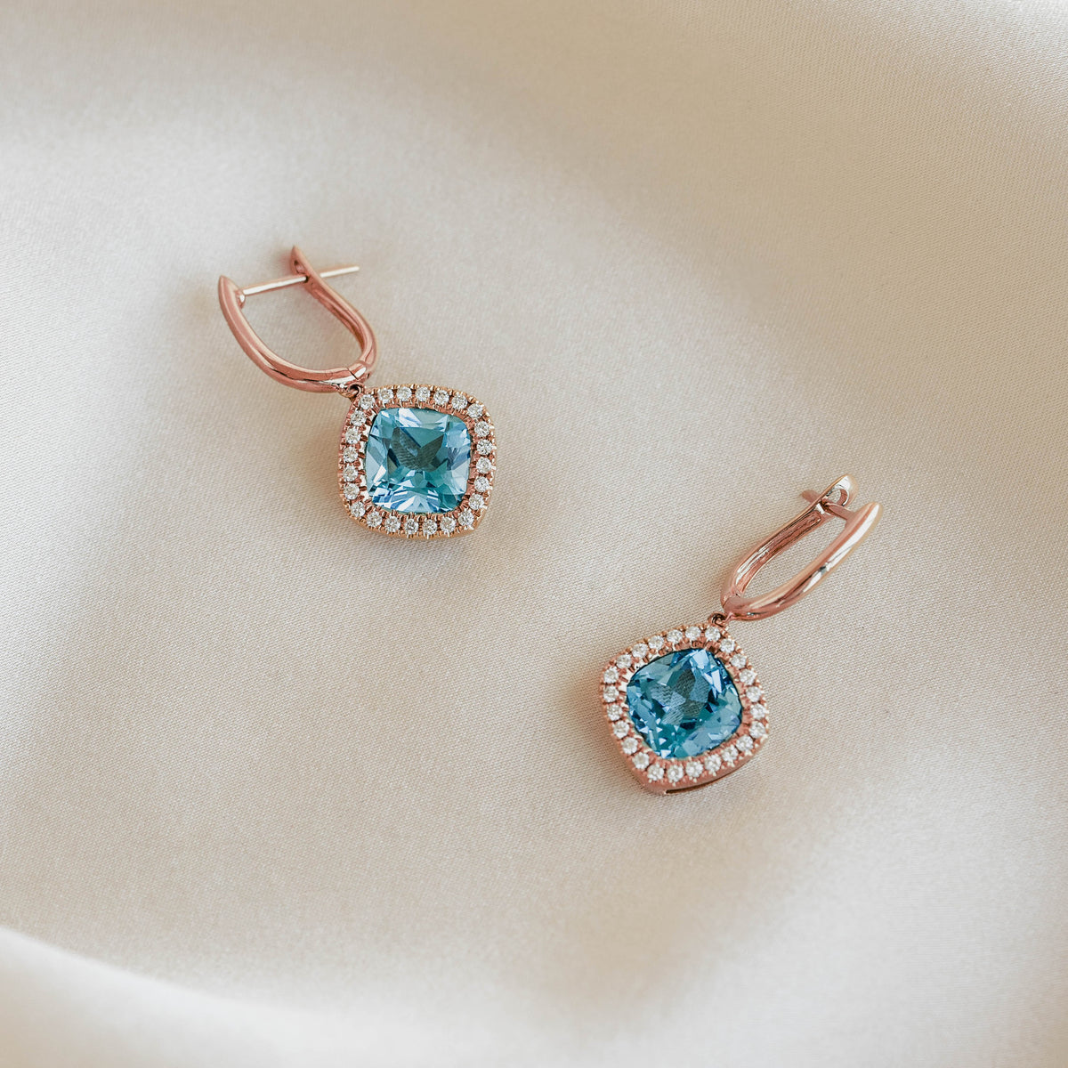 Swiss Blue Topaz and Diamond Halo Drop Earrings Rose Gold - Elvira on soft beige fabric background in natural light