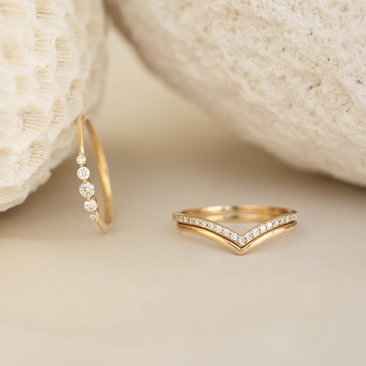 Close-up of V Ring 14k Gold - Malva chevron ring with small diamonds on a beige surface between textured stones