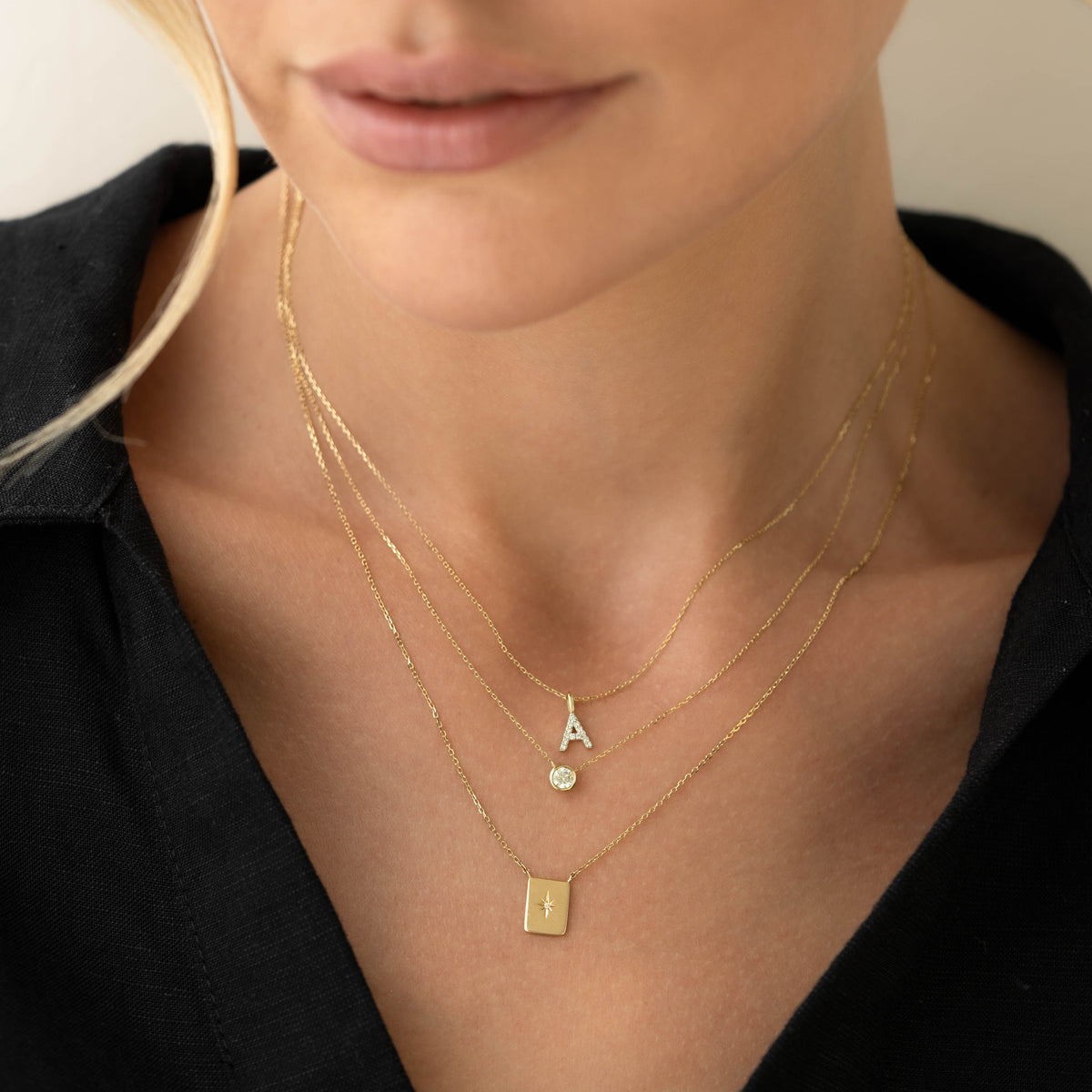 Close-up of a woman wearing layered gold necklaces including the Bezel Set Diamond Necklace 14k Gold - Ulla with a black top