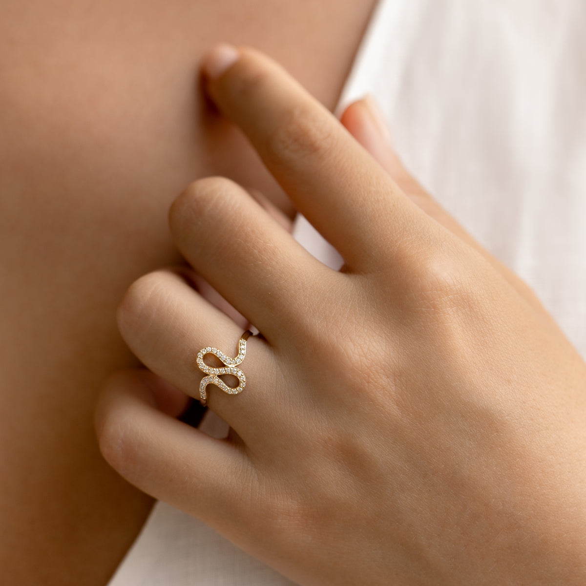Close-up of a hand wearing the Diamond Squiggle Ring 14k Gold with pavé set diamonds on smooth skin background