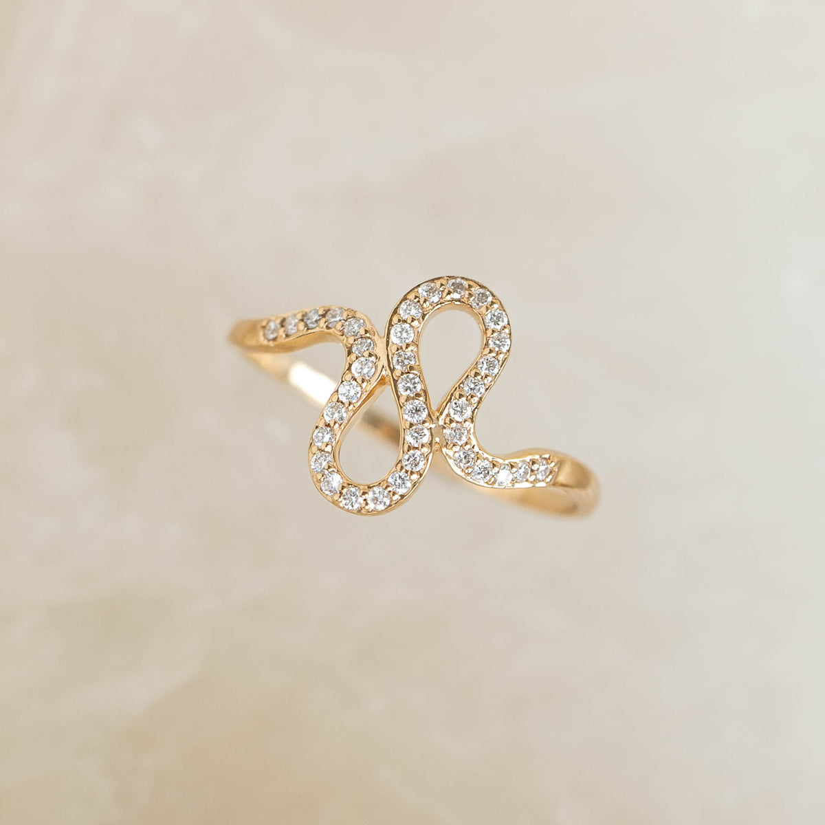 Close-up of Diamond Squiggle Ring 14k Gold with pavé set diamonds on a wavy 14k gold band on a beige background