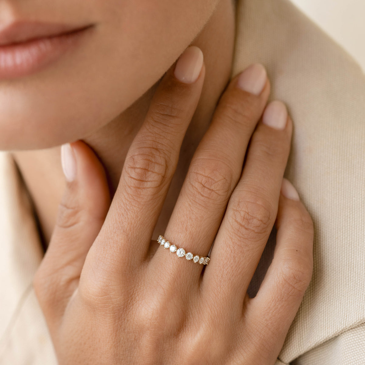 Close-up of a hand wearing the Graduated Diamond Ring 14k Gold - Giselle with eleven round diamonds on a light background