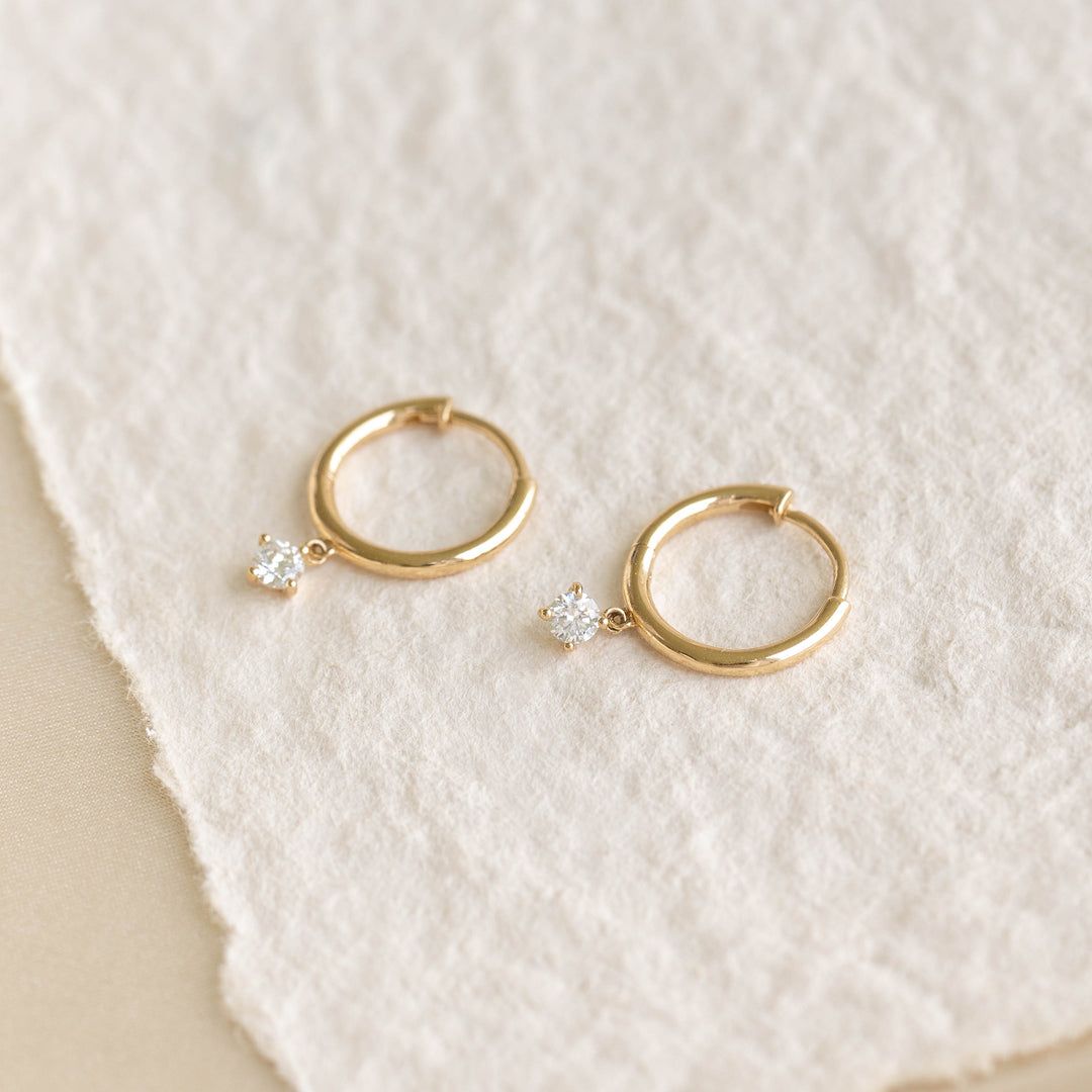 Close-up of Diamond Drop Huggie Earrings 14k Gold - Joleen featuring 14k gold hoops with sparkling diamond drops on a textured background