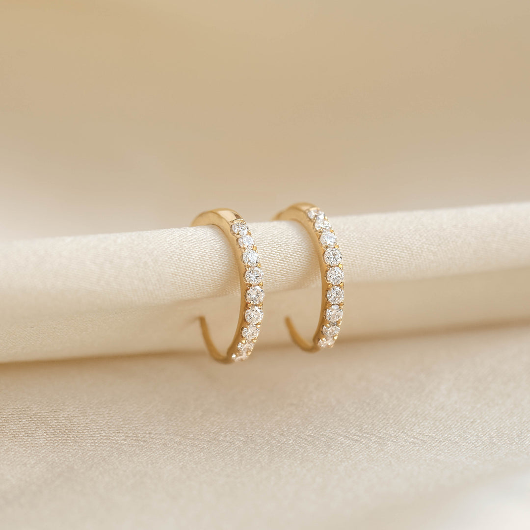 Close-up of Pave Diamond Huggie Earrings 14k Gold - Oceane showcasing pavé set diamonds on a beige fabric background
