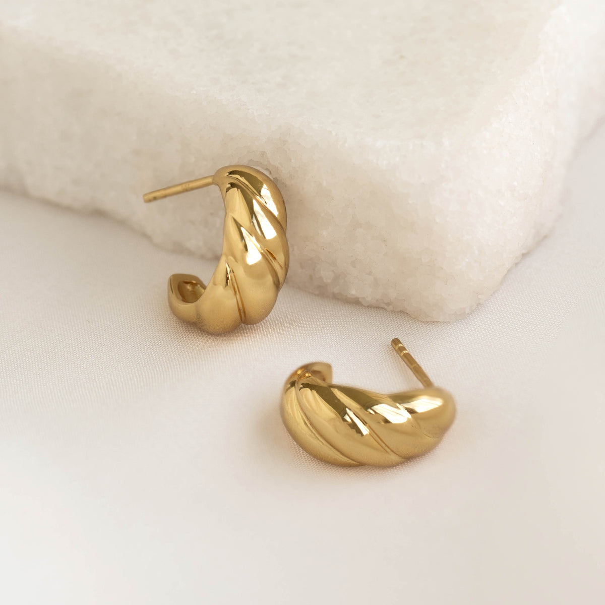 Close-up of gold vermeil Croissant Earrings - Piper with a twisted design on a soft beige fabric background