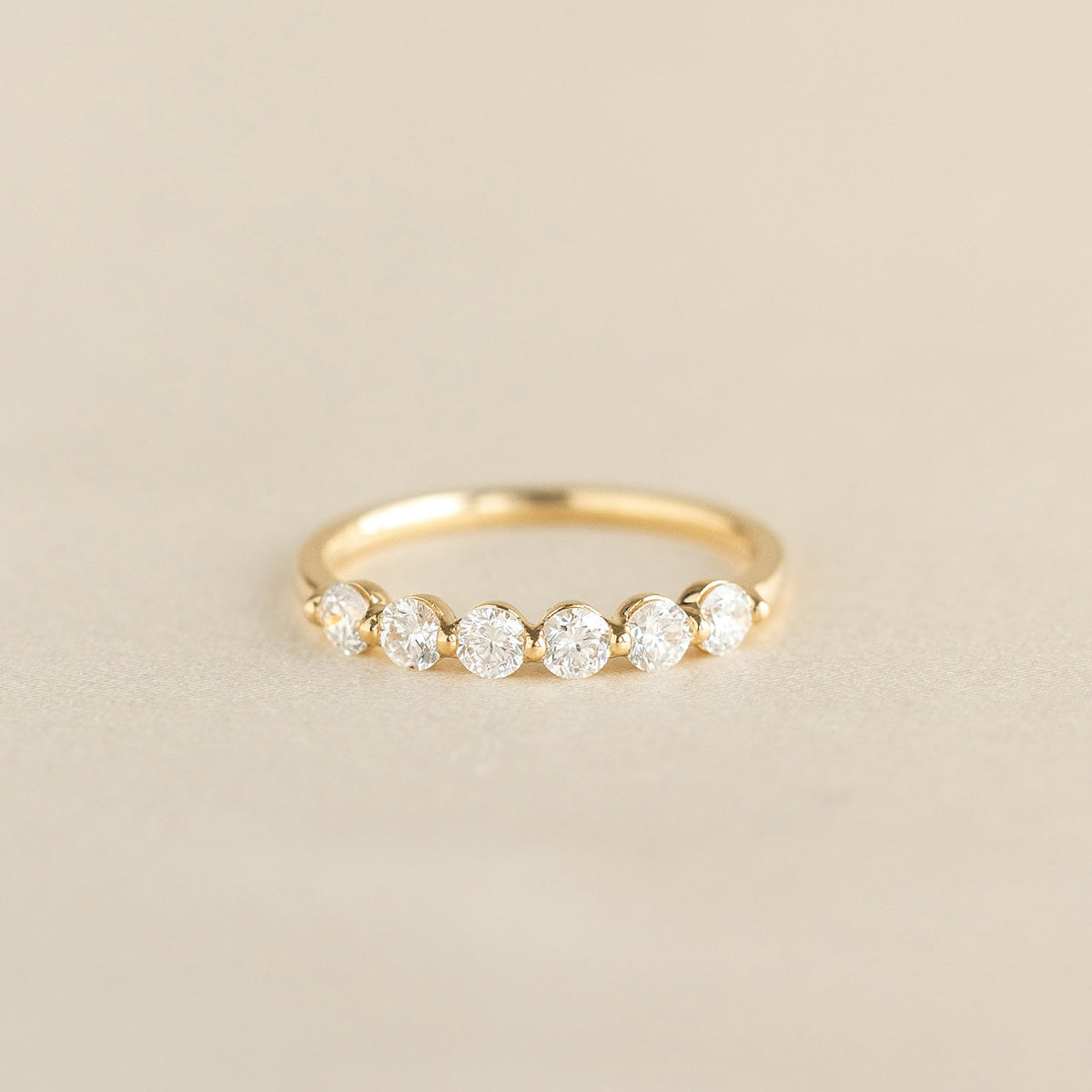 A delicate Yellow Gold ring featuring a round diamonds set along the band, displayed on a soft beige background.