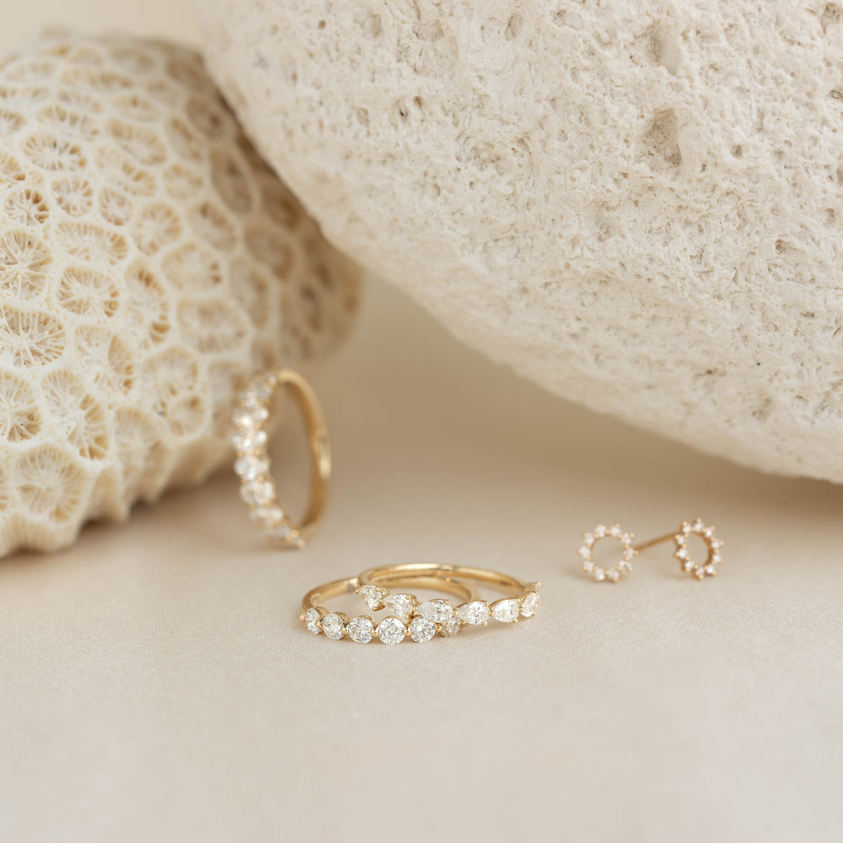 Three delicate Yellow Gold rings with diamond settings are displayed on a soft beige surface.