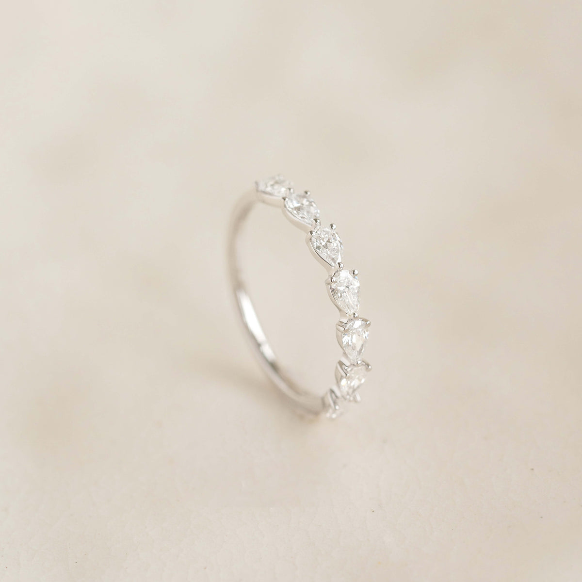 A delicate White Gold ring displayed upright, featuring a row of alternating pear cut diamond set along the band.