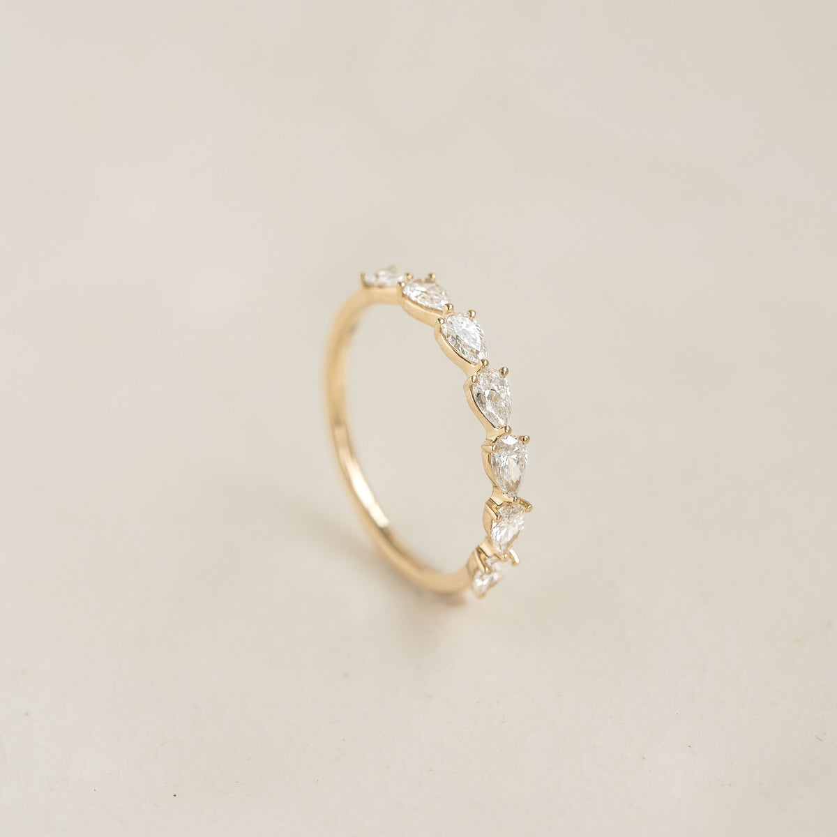 A delicate Yellow Gold ring displayed upright, featuring a row of alternating pear cut diamond set along the band.