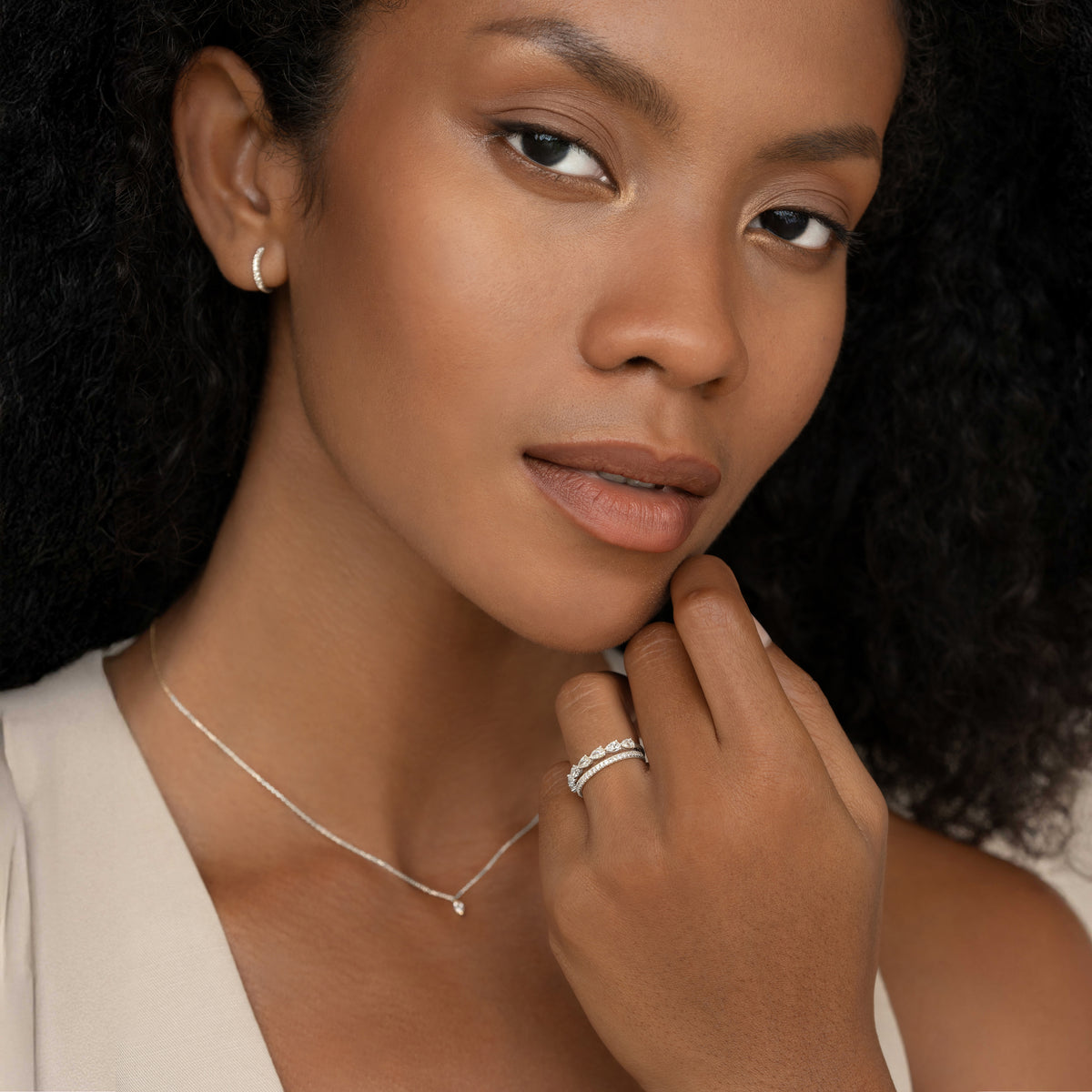 A close-up portrait of a model wearing a delicate White Gold diamond ring with alternating pear-cut.