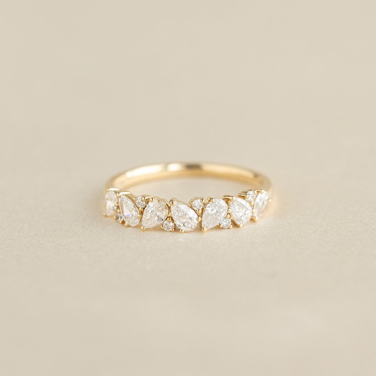 A delicate Yellow Gold ring featuring a row of alternating pear-shaped and round diamonds set along the band, displayed on a soft beige background.