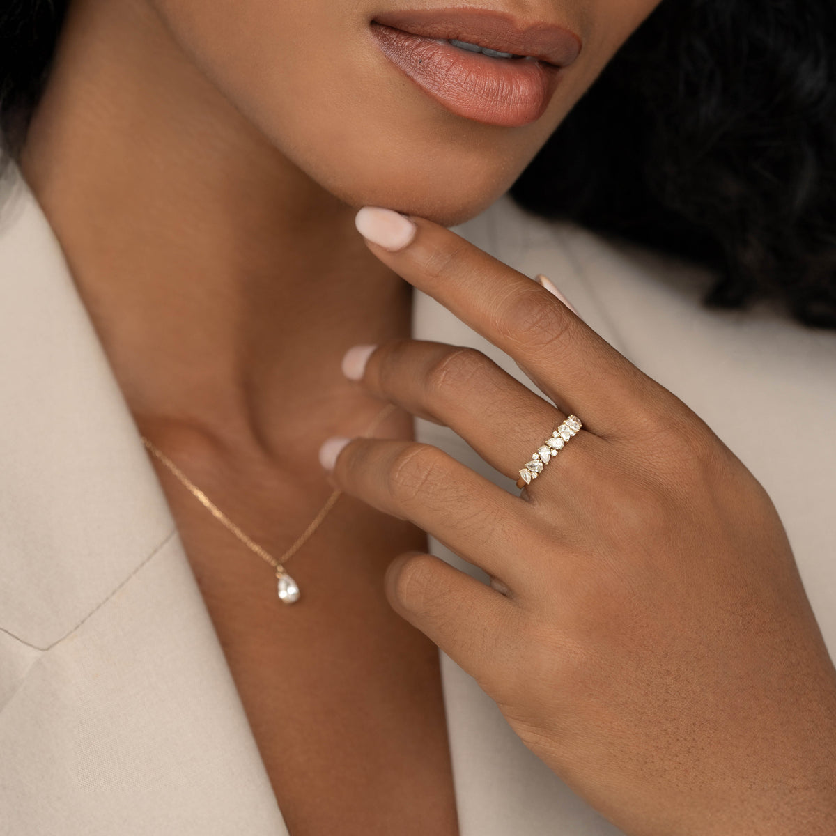 A close-up of a model wearing a delicate Yellow Gold diamond ring with alternating pear-shaped and round stones, her hand resting near her chin.