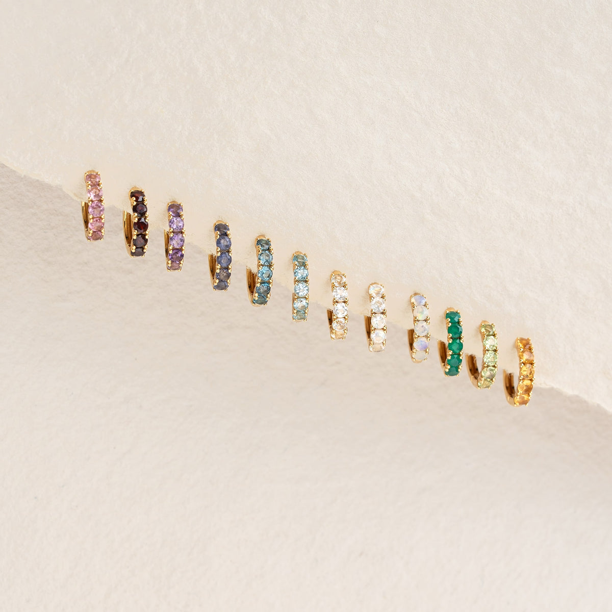 February Birthstone Huggie Earrings - Amethyst displayed with various gold vermeil gemstone huggie styles on light background