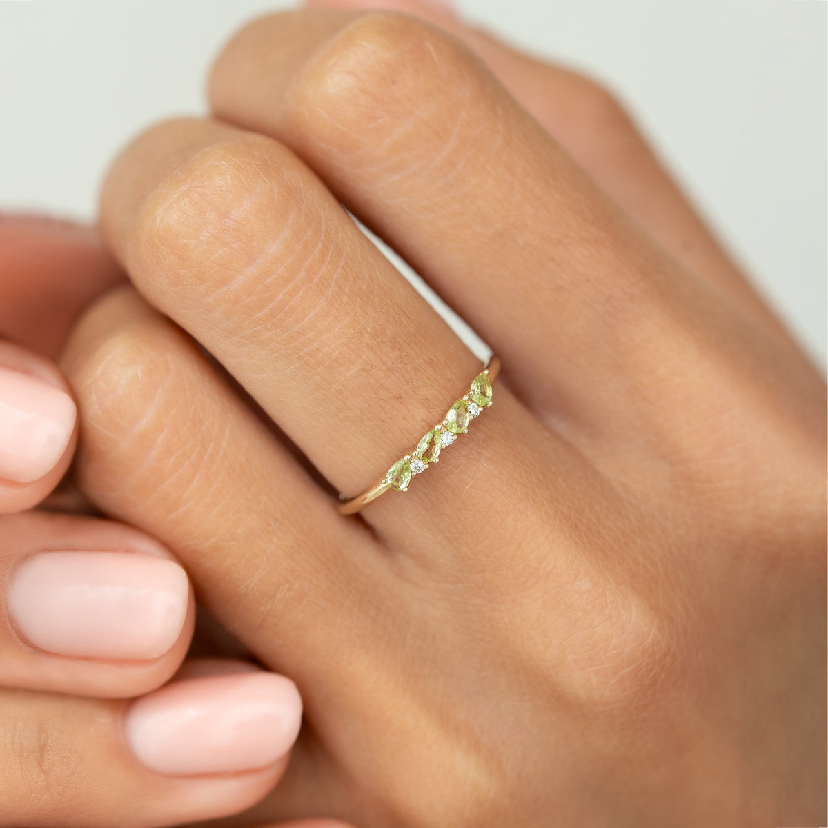Close-up of a hand wearing the August Birthstone Pear Ring 14k Gold - Olivine and Diamond with pear cut stones and round diamonds.