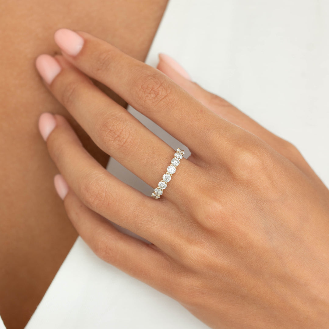 Hand of a woman wearing a delicate Yellow Gold ring set with round cut diamonds, styled on the ring finger against a soft neutral background.