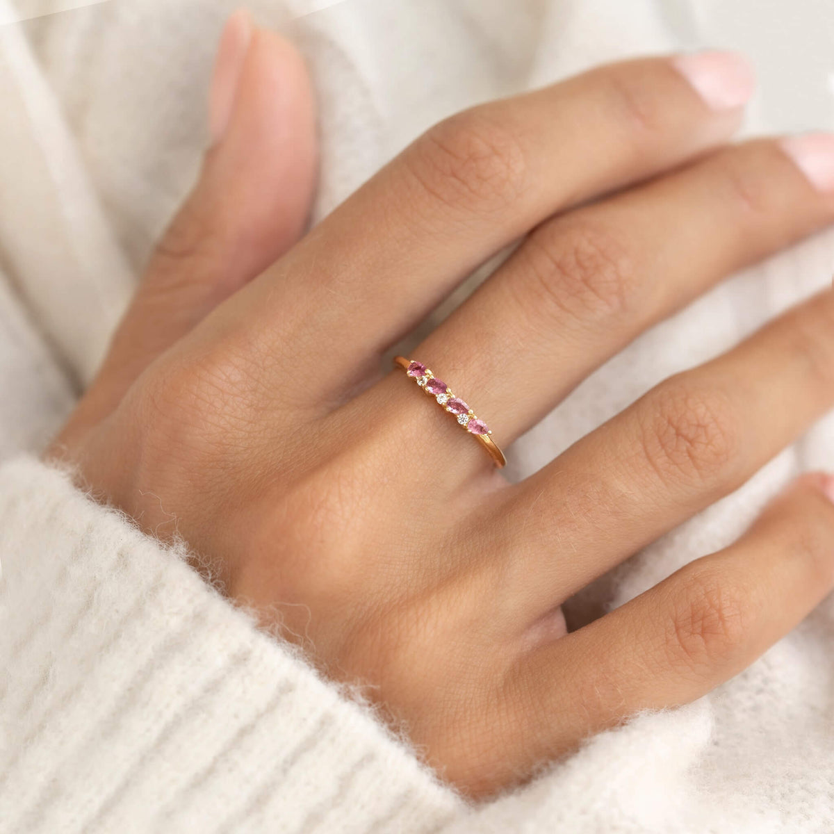 Close-up of a hand wearing the July Birthstone Pear Ring 14k Gold - Pink Tourmaline and Diamond on a cozy cream sweater background