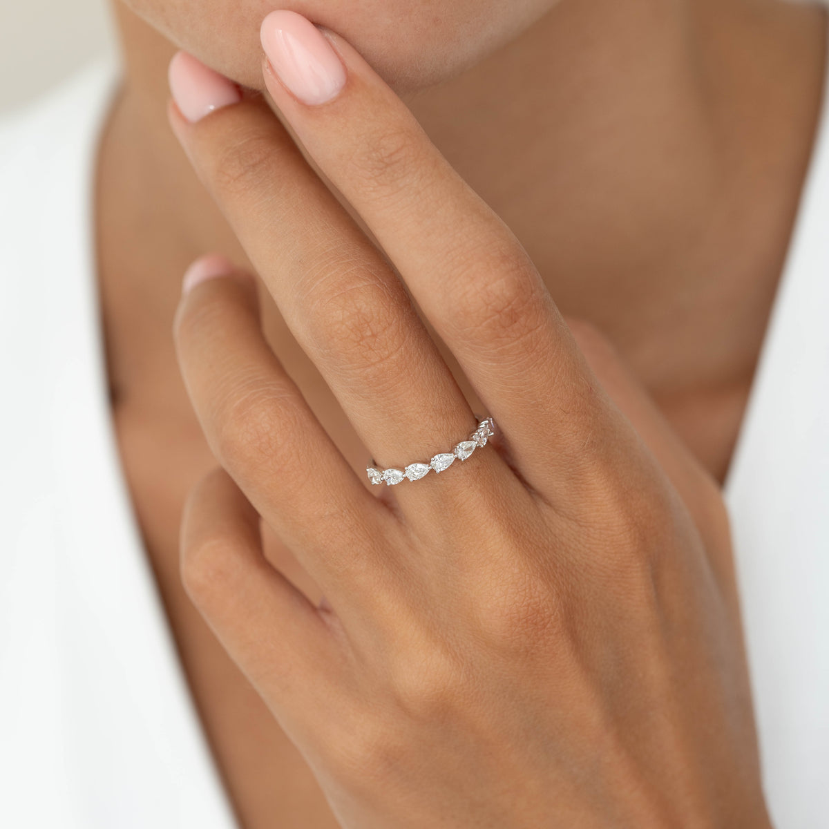 A close-up of a hand wearing a delicate White Gold ring set with alternating pear-cut diamonds.
