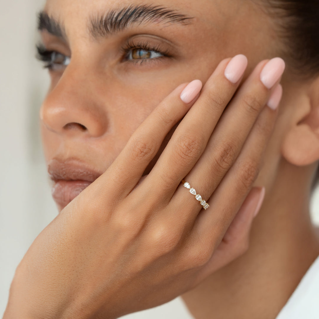A close-up portrait of a model wearing a pear cut diamond ring, with her hand on her face.