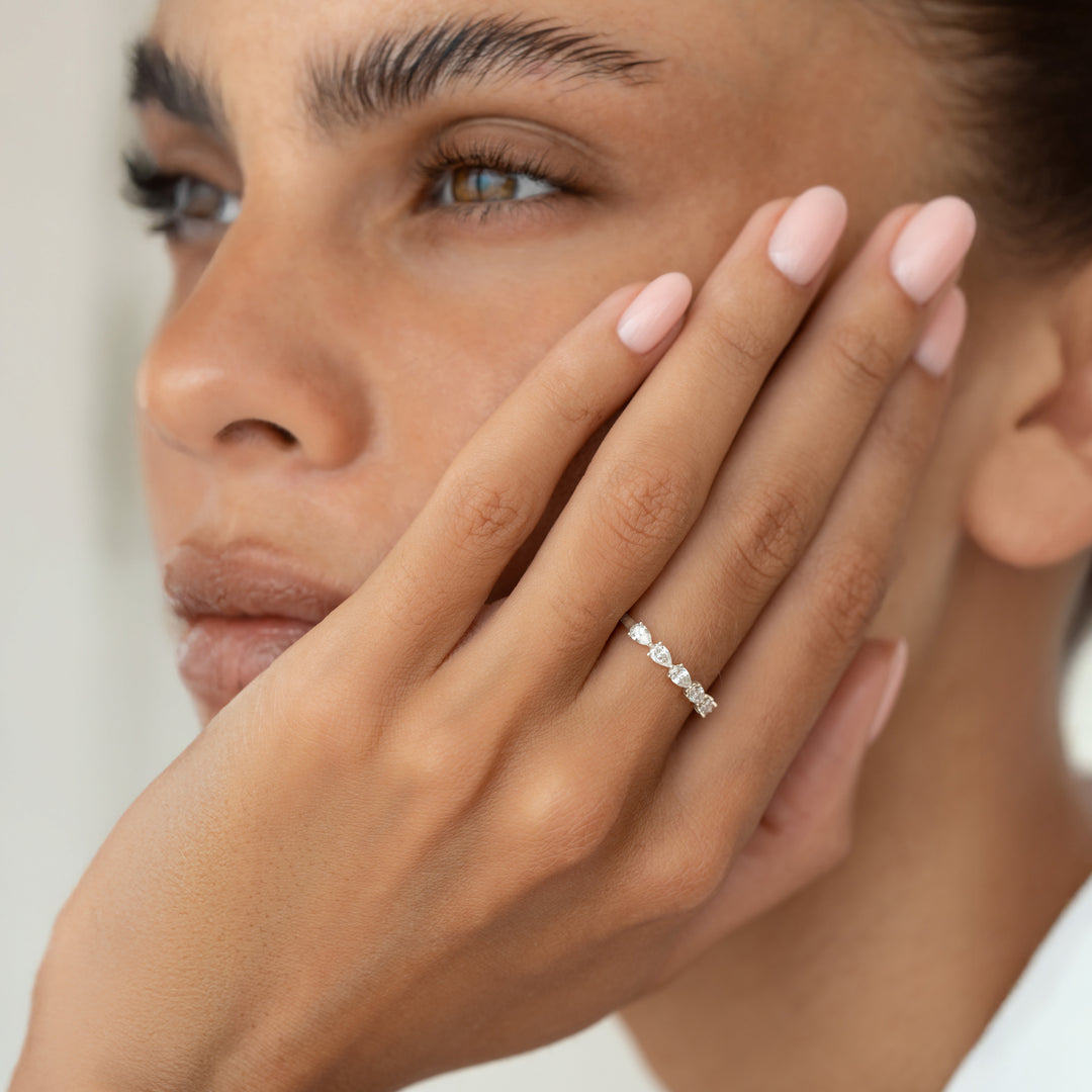 A close-up portrait of a model wearing a pear cut diamond ring, with her hand on her face.