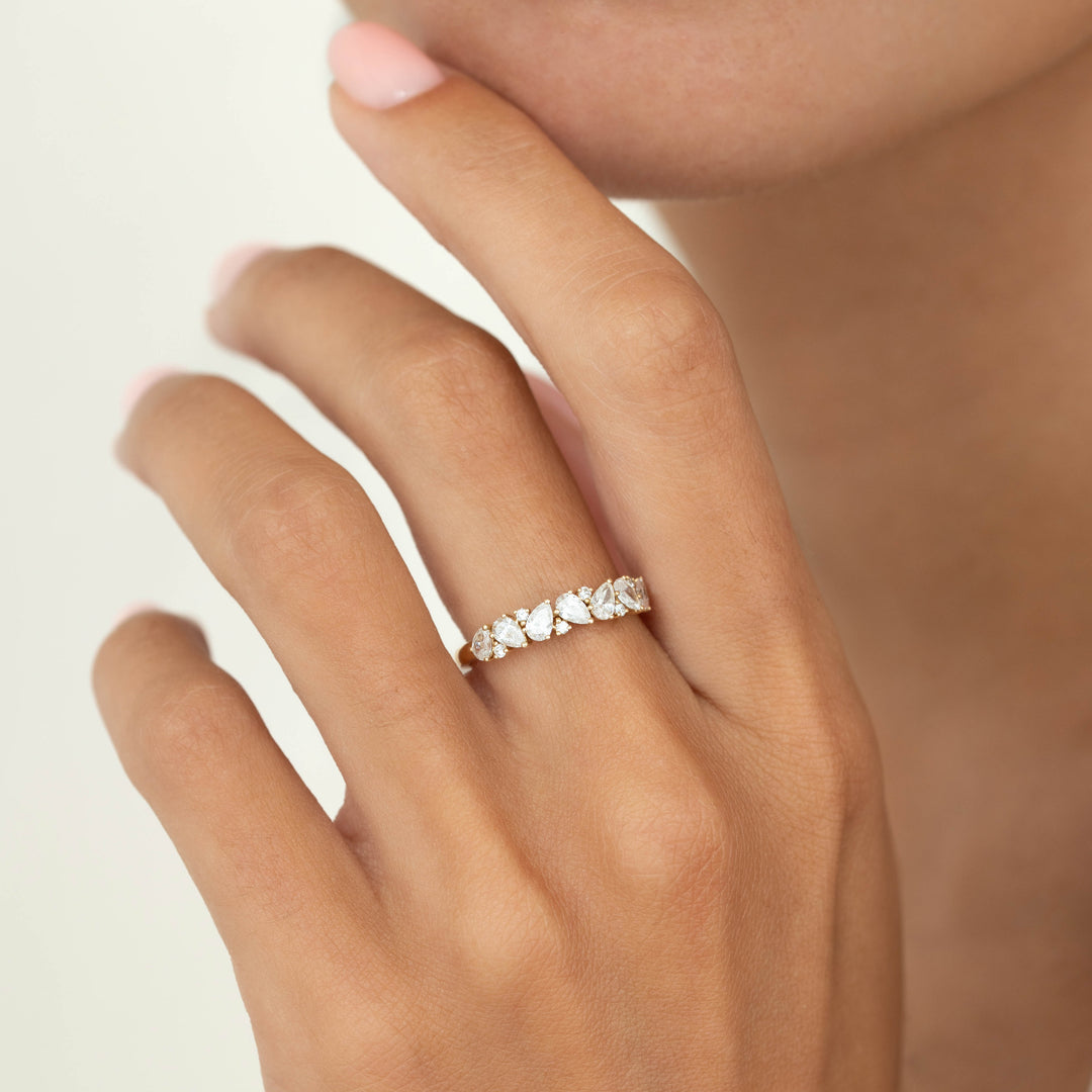 A close-up of a hand wearing a delicate Yellow Gold ring set with alternating pear-shaped and round diamonds, styled on the ring finger against a soft neutral background.