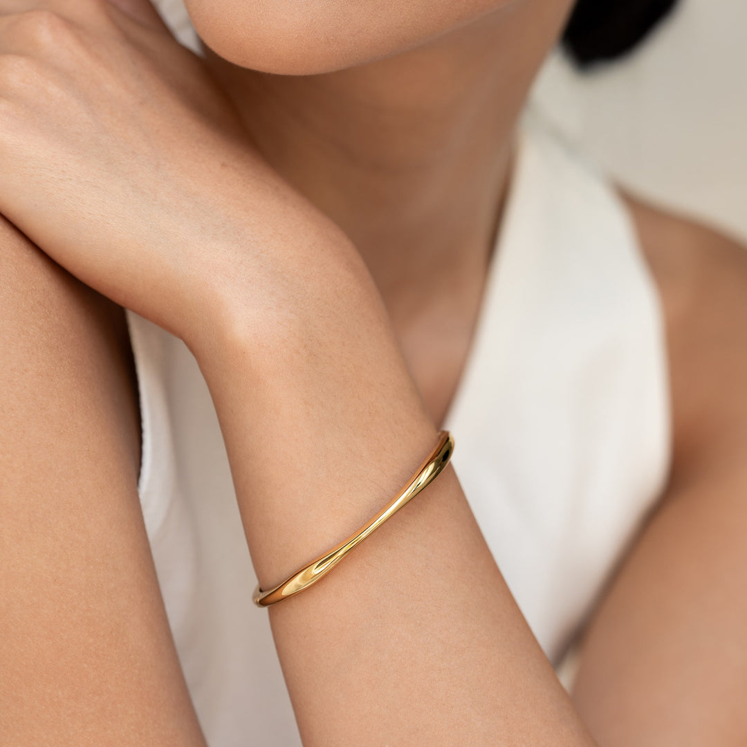Close-up of a woman wearing the Gold Organic Bangle S - Aelia with a sleek asymmetrical gold vermeil design on her wrist