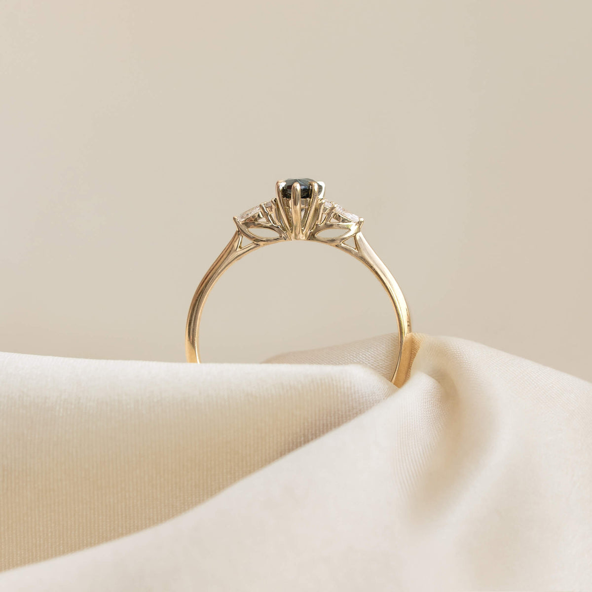A studio photograph captures the profile view of the yellow Gold ring, positioned upright as if emerging from a soft, undulating white fabric surface.