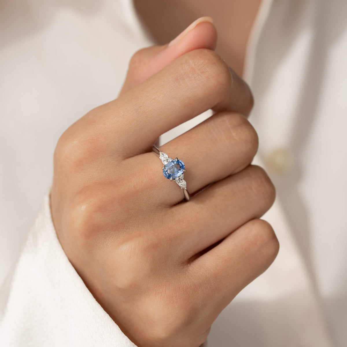 The hand is elegantly posed against a soft, off-white or cream-colored fabric sleeve, highlighting how the White Gold ring looks when worn.