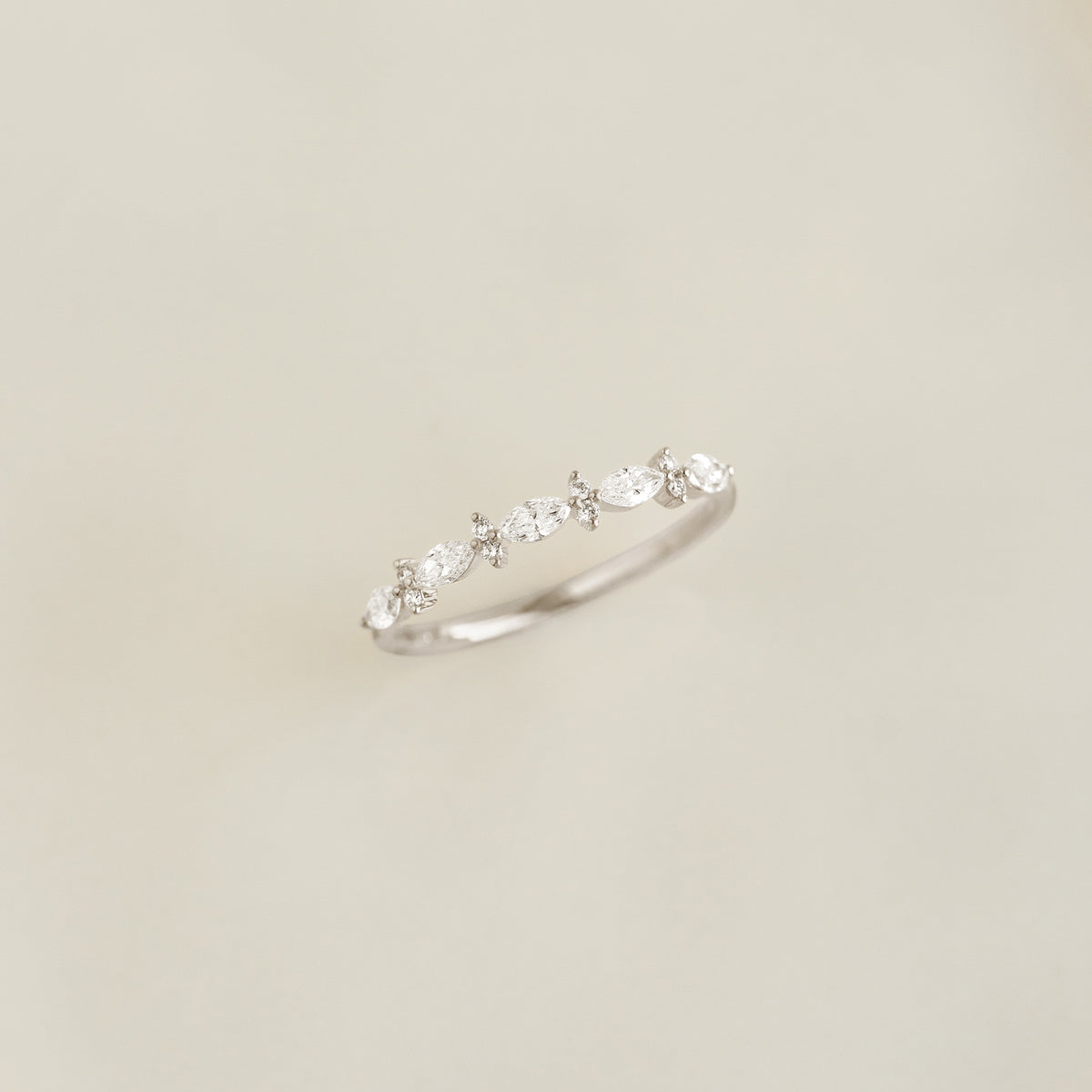 Close-up of Marquise and Round Diamond Ring White Gold - Aurelia with sparkling diamonds on a light beige background