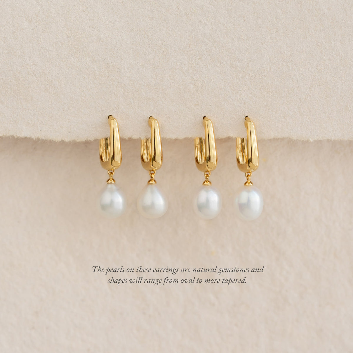 Close-up of four Pearl Drop Hoop Earrings - Maeve with gold vermeil and freshwater pearl drops on a beige background