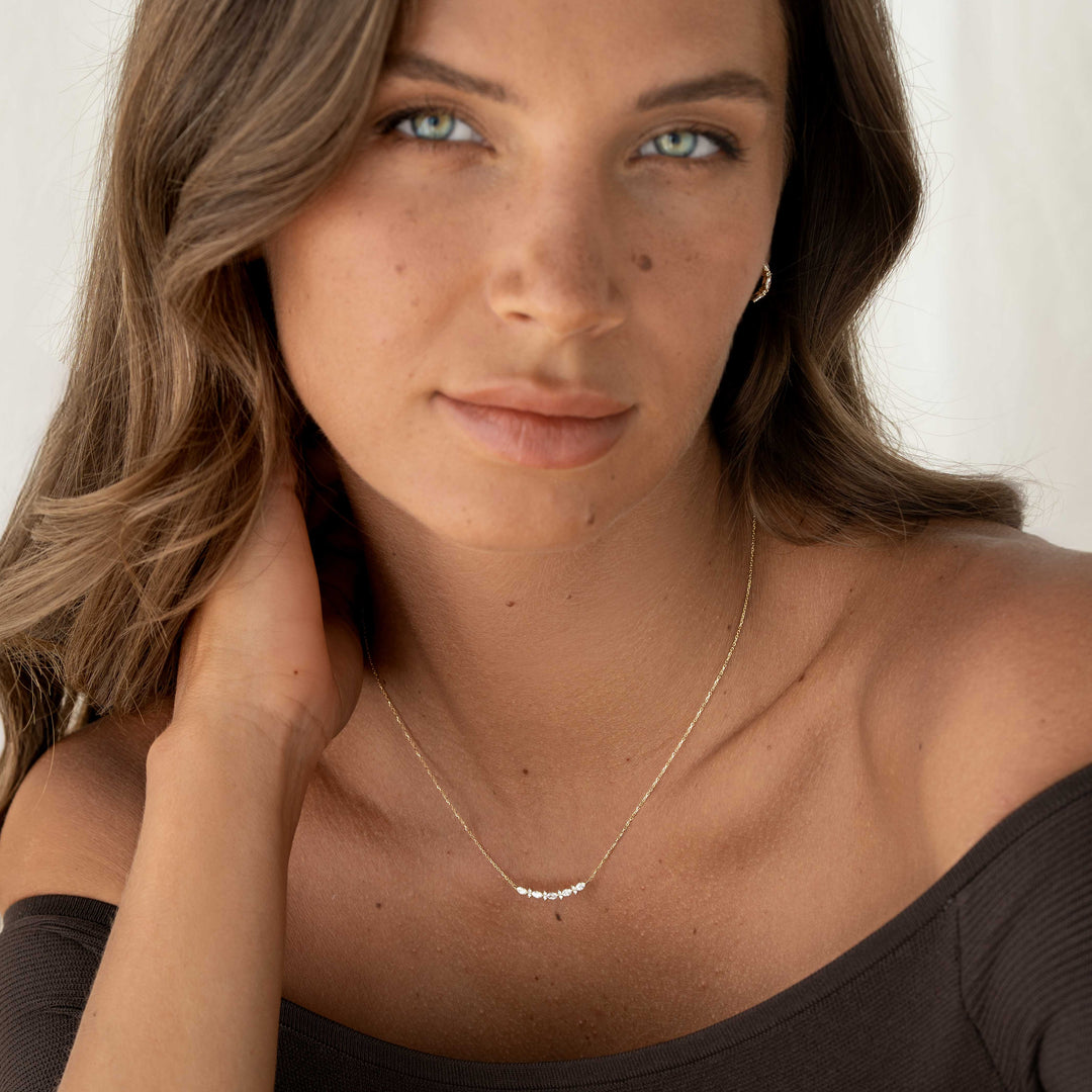 Close-up of a woman wearing the Marquise and Round Diamond Necklace 14k Gold - Noelia with a black off-shoulder top against a neutral background
