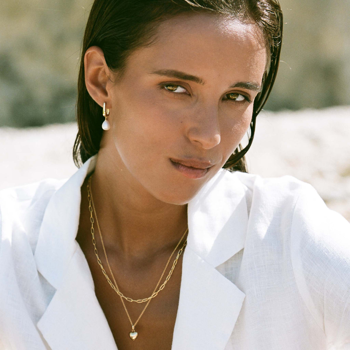 Woman wearing Pearl Drop Hoop Earrings - Maeve with layered gold necklaces and white linen shirt outdoors in natural light