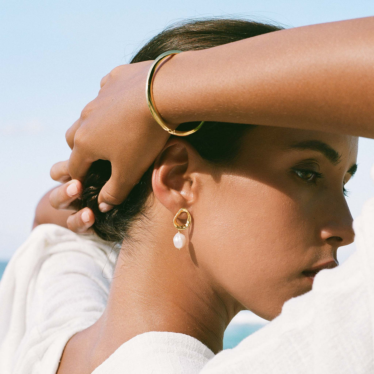 Side profile of a woman wearing Gold Organic Bangle S - Aelia with sculptural gold and pearl earrings outdoors