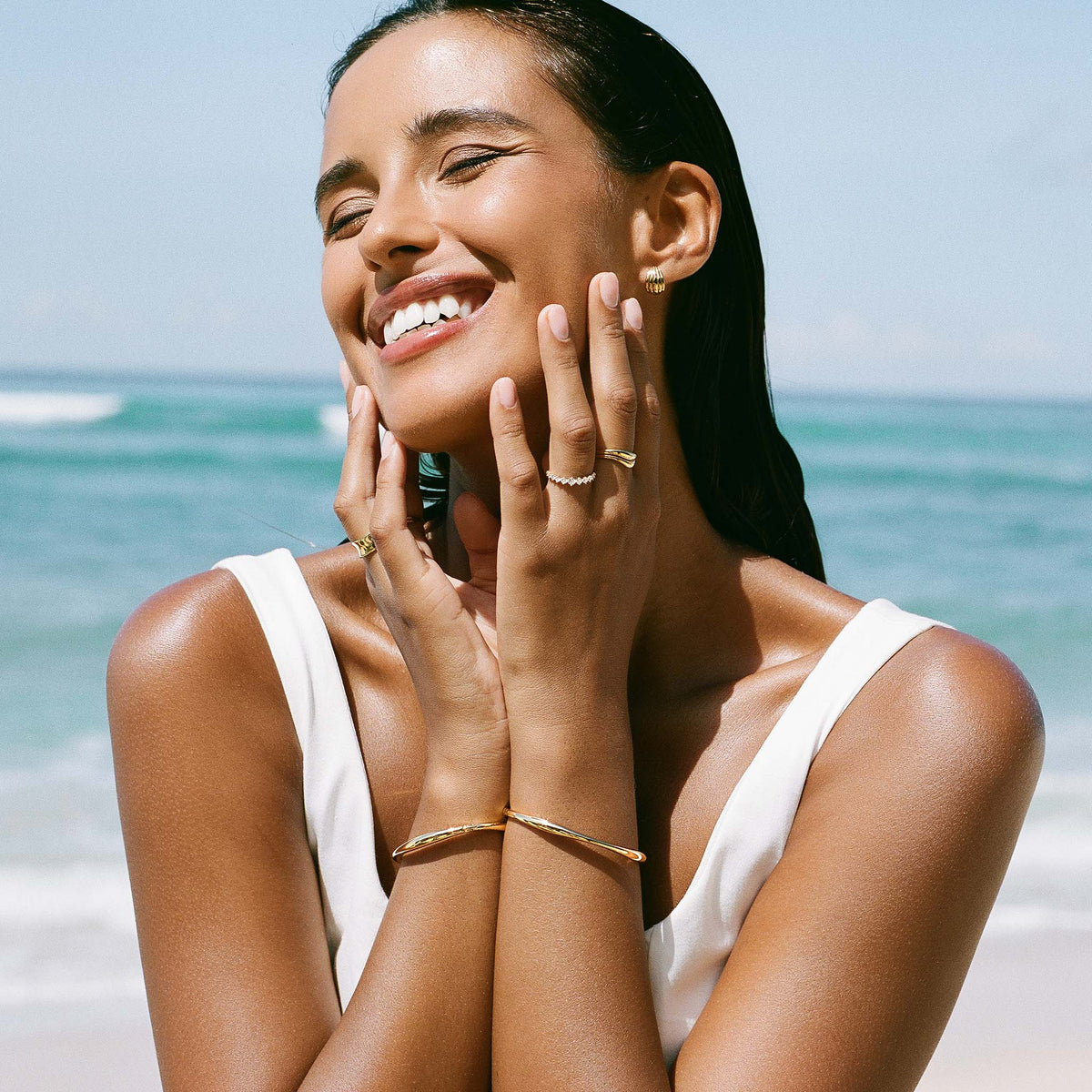 Woman smiling at the beach wearing a white tank top and Gold Organic Bangle S - Aelia on her wrist