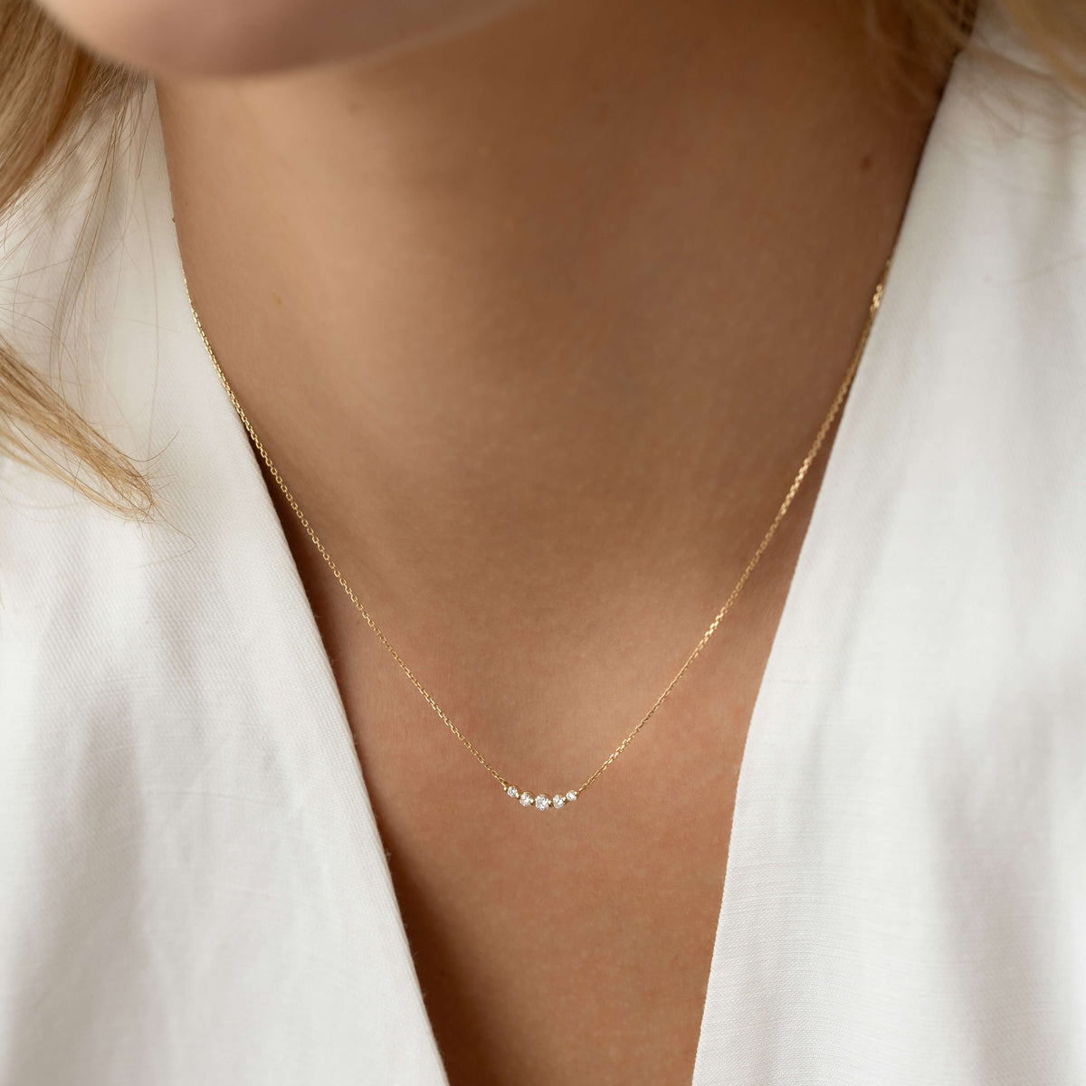 Close-up of a woman wearing the Diamond Curved Bar Necklace 14k Gold - Elodie with five graduated diamonds on a gold chain