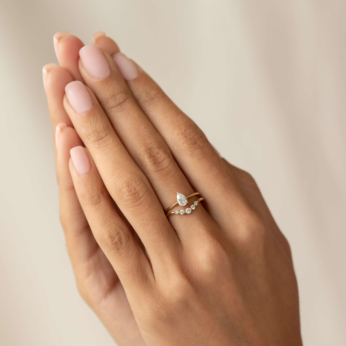 Hands featuring an elegant Gold ring with a teardrop diamond and smaller gems. Soft lighting, calm and refined atmosphere.
