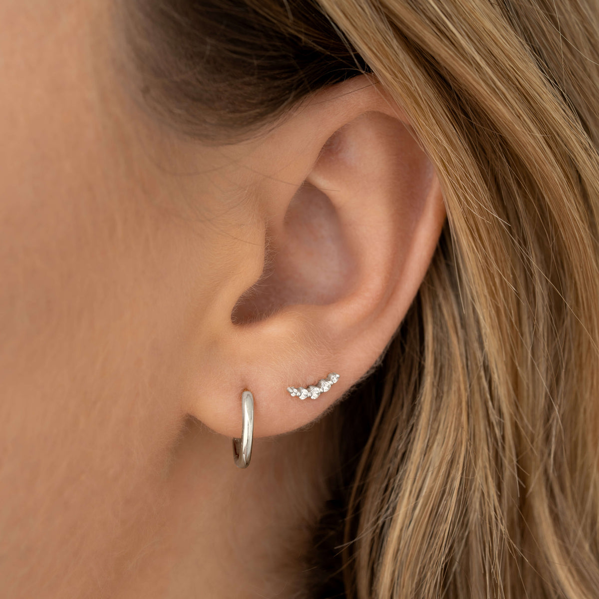 Close-up of an ear wearing Diamond Climber Stud Earrings White Gold - Rhea showing a curved row of sparkling diamonds