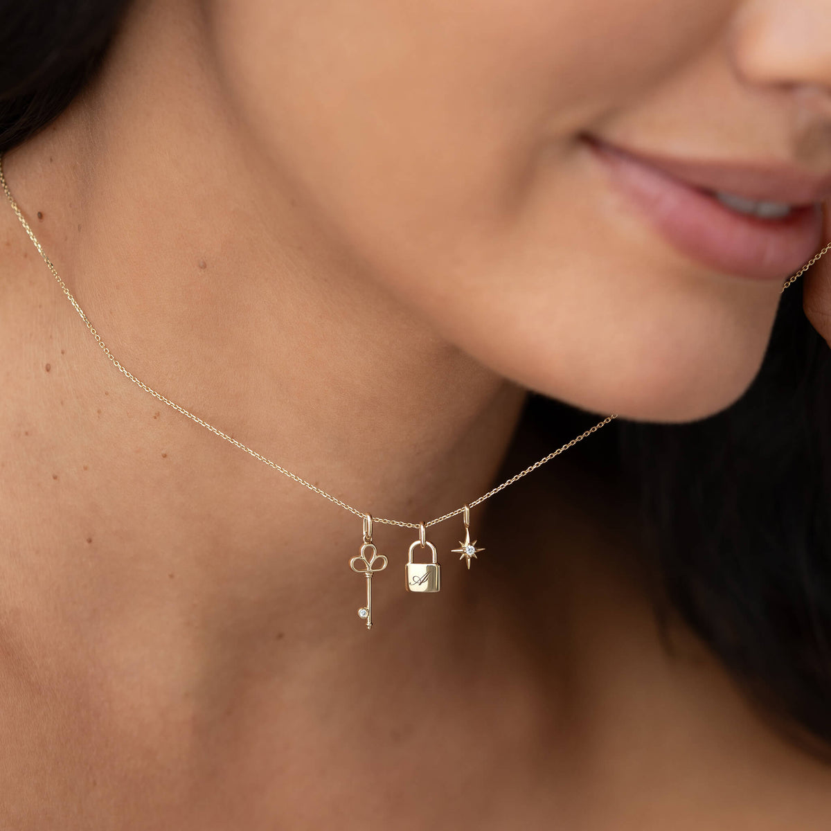 Close-up of a model wearing a delicate Yellow Gold necklace with three dangling charms: a key, a padlock, and a star charm.