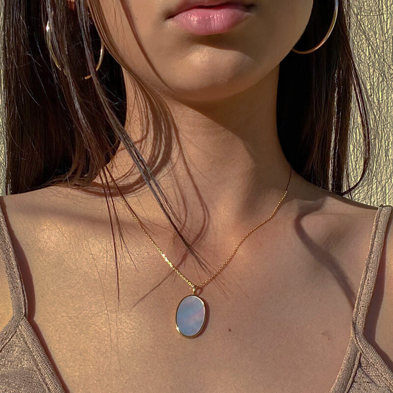 Close-up of a woman wearing a gold oval pendant necklace and large gold hoop earrings with natural sunlight shadows
