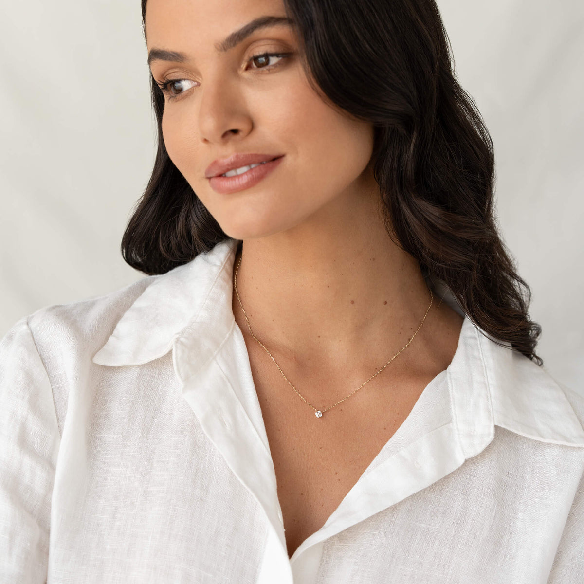 Portrait of a woman in a white blouse wearing a delicate Gold necklace with a small asscher-cut gemstone pendant.