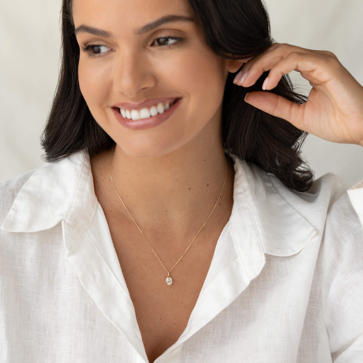 Model wearing a delicate Yellow Gold necklace with a small oval shaped pendant, styled with a white collared shirt.