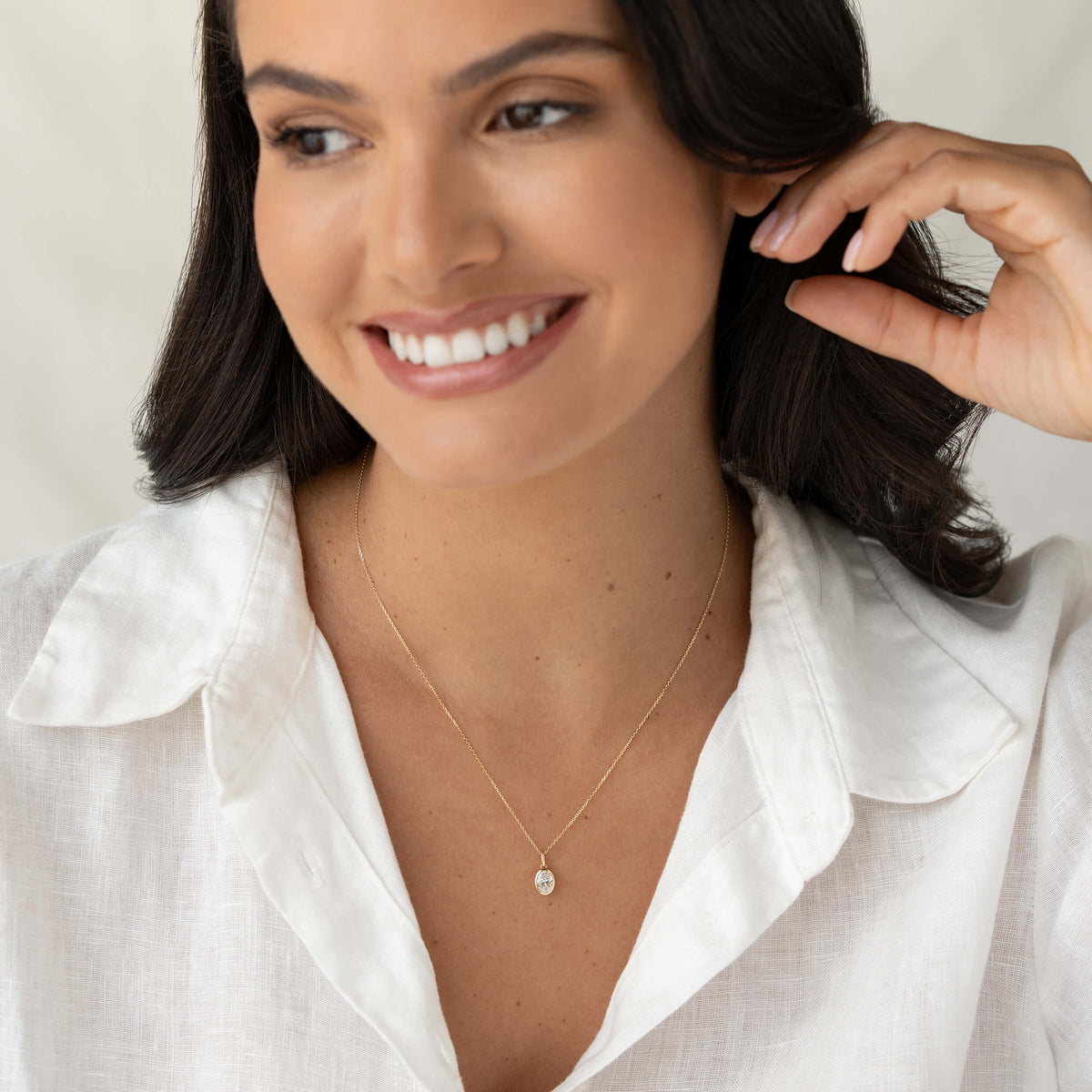 Smiling woman wearing a delicate Yellow Gold necklace with a small diamond pendant, dressed in a white blouse against a soft neutral background.