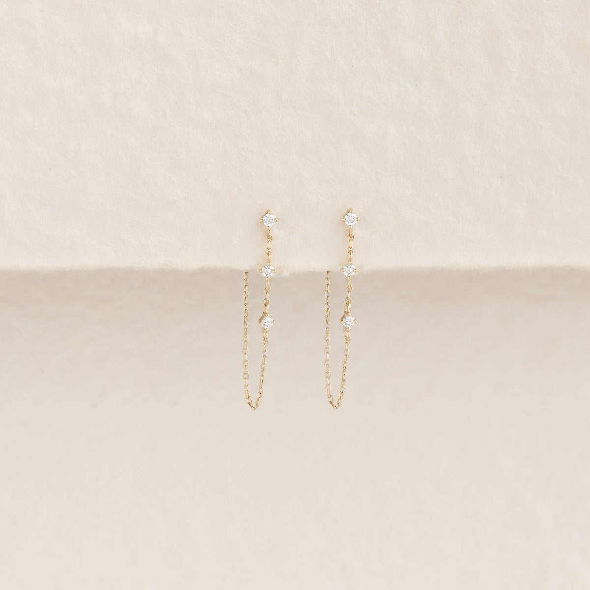 Elegant Gold chain earrings with small diamonds, displayed against a soft cream background. The minimalist design exudes a delicate, refined elegance.