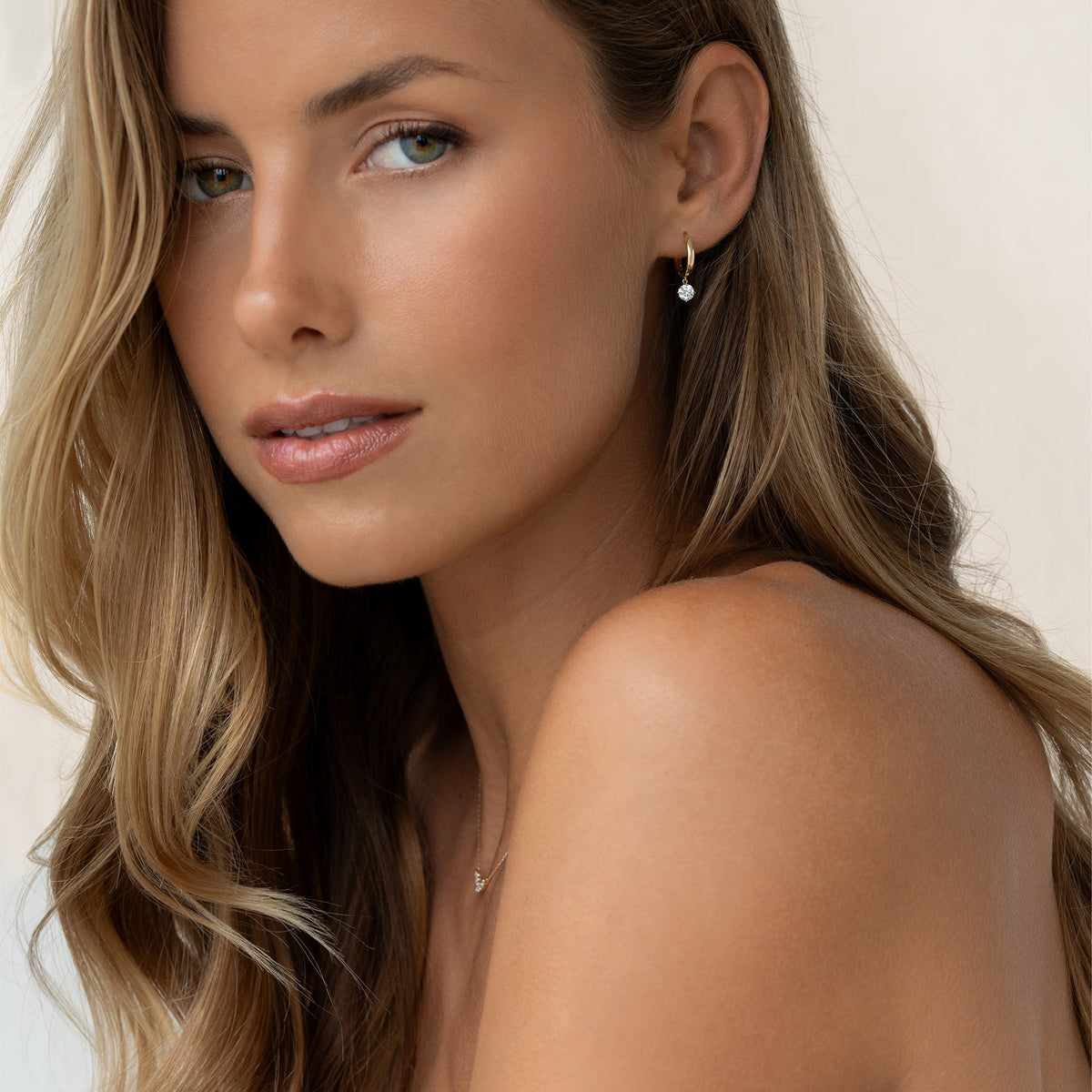 A lovely woman, displaying her 14k gold diamond drop huggie earrings with long flowing hair.