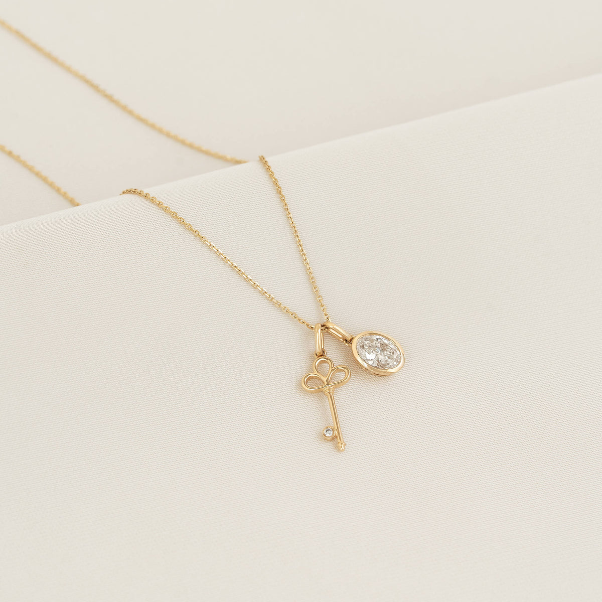 Yellow Gold necklace featuring a key-shaped charm with a small diamond accent and a oval diamond pendant, displayed on a white textured surface.