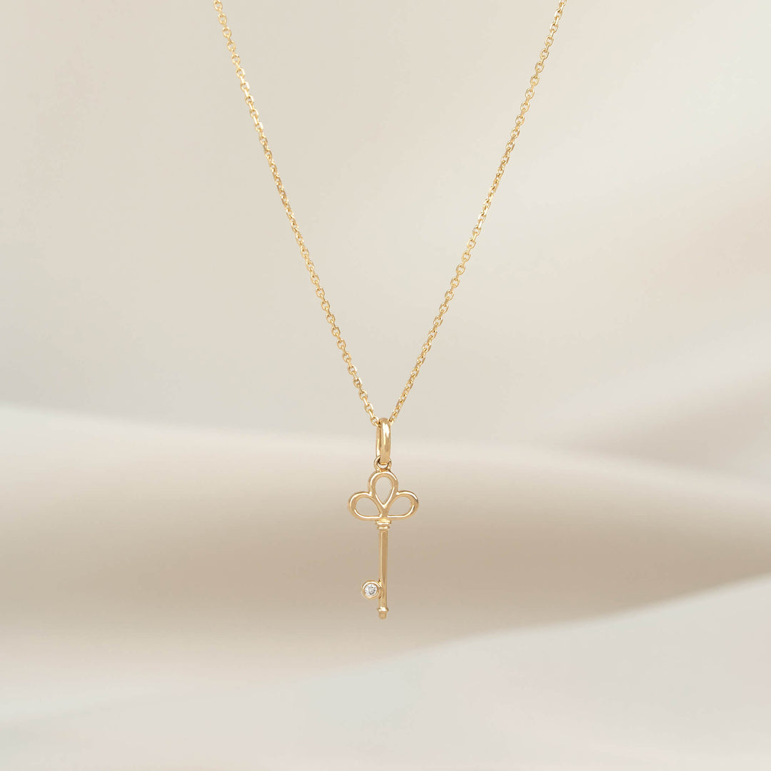 Yellow Gold necklace with a polished key shaped pendant, displayed on a delicate chain against a soft neutral background.