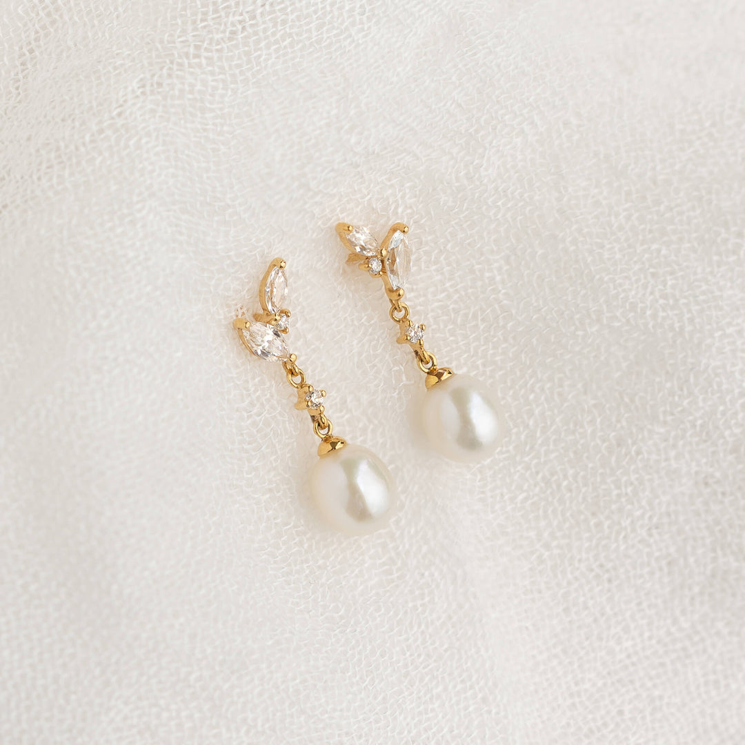 Elegant gold earrings with pearl and crystal accents rest on delicate white lace, exuding a sense of sophistication and classic beauty.