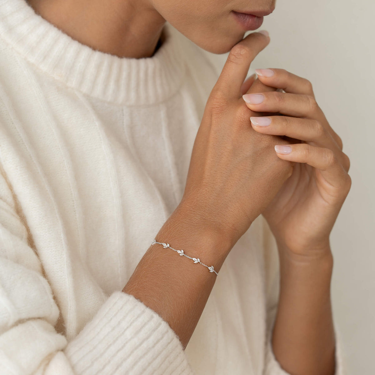Close-up of a person wearing a delicate bracelet with sparkling stones along a fine chain, paired with a cream knit sweater.