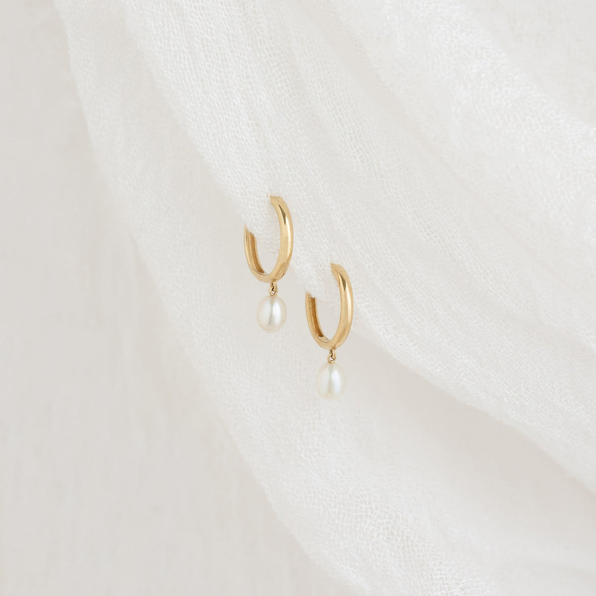 Stylish huggie earrings in 14k gold, adorned with a pearl drop for a refined and elegant appearance.