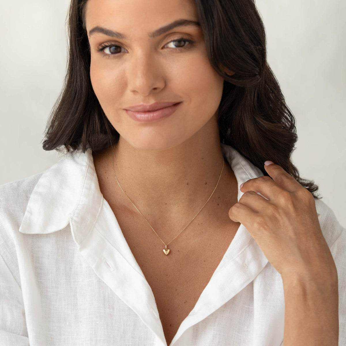Model wearing a delicate Yellow Gold necklace with a small heart-shaped pendant, styled with a white collared shirt.
