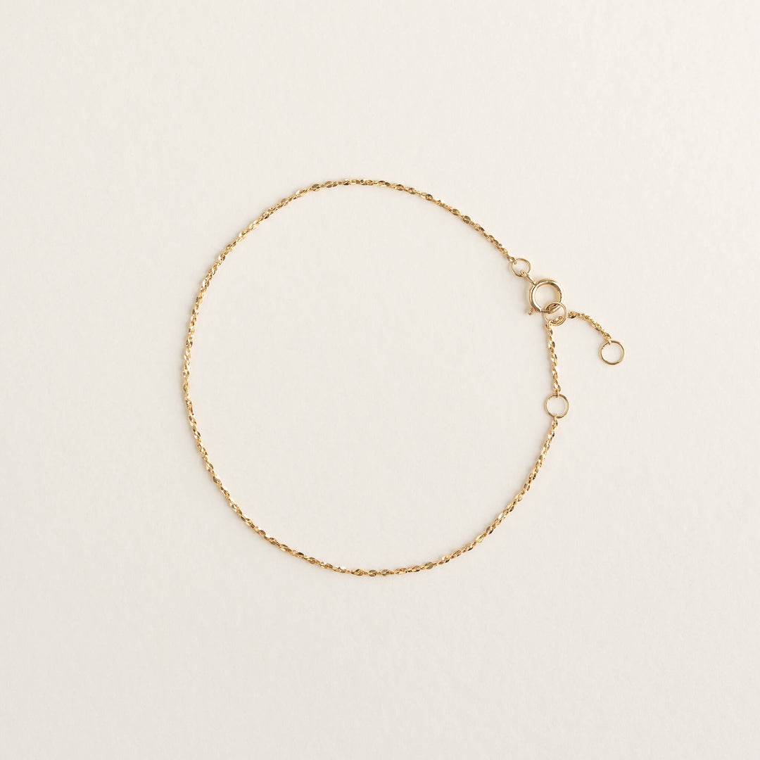 A delicate Gold chain bracelet with a clasp and adjustable links lies flat on a light beige background, conveying elegance and simplicity.